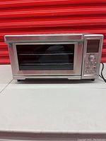 Front view of the stainless steel convection toaster oven showing the glass door, handle, control panel with buttons, dial and digital display