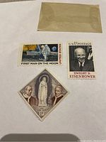 Three stamps laid flat: First Man on the Moon, Dwight D. Eisenhower, and Monaco religious stamp