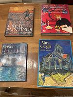 Four art coffee table books arranged on a wooden table showing the covers of 'Great Paintings of the Western World,' 'Impressionism and Post-Impressionism,' 'Essential Monet,' and 'Van Gogh' by Frank Milner.