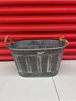 Side view of the galvanized steel planter basket with visible twine handle and vertical embossed stripes on the outer surface.