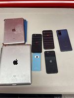 Top view of 2 iPads, 3 iPhones, 1 Samsung phone, and unknown blue device lying on a surface.