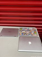 Three closed laptops on table against red background: two Asus and one Apple MacBook Pro