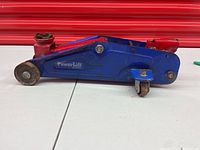 Side view of blue and red Power Lift hydraulic jack missing the lifting arm, showing wheels and body details.