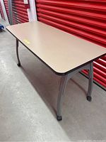 Full side view of rectangular desk/table with beige top and gray legs with caster wheels, showing top and one side.