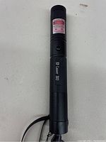 Black SD Laser 303 pocket laser pointer with on/off button, label, and hand strap on a white surface.