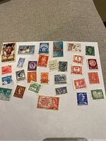 Varied vintage postage stamps arranged on a white sheet, showing different countries, denominations and colors including King George VI and Queen Elizabeth II.
