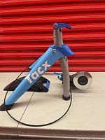 Side view of the blue Tacx branded frame with resistance roller and adjustment cable.