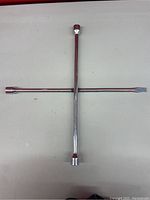 Metal tire iron laid out in a cross shape showing four socket ends and flat pry bar on white background.
