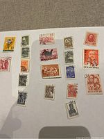 Top view of multiple small vintage stamps scattered on a fabric surface showing various designs including flowers, birds, people, and Cyrillic text.