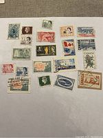 A group of 19 vintage Canadian postage stamps including Queen Elizabeth II portraits, Canadian flags, Expo '67 commemoratives, and various historical and cultural themes, displayed on a beige fabric background.