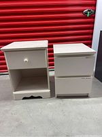 Both white side tables standing side by side on concrete floor, showing their fronts and general condition.