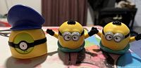 Three Minion toys including one with a blue cap and two with goggles and gloves, all yellow, on a flat surface.