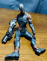 Action figure of a male cyborg in detailed blue and brown armor with a futuristic gun, seated on a wooden surface