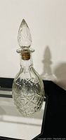 Clear crystal decanter with detailed cut glass design and matching stopper shown against a white wall and mirrored surface.