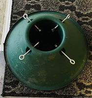 Overhead view of a green metal Christmas tree stand with four eye bolts for holding and securing a Christmas tree trunk.