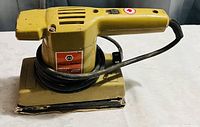 Photo of a yellow Black & Decker electric sander with power cord wrapped around the base, showing the side with label and ventilation.