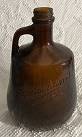 Brown glass antique bottle with embossed advertising text 'Goodenhams ESTD 1832' and a handle on the side.