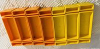 Eight vintage Fisher-Price rectangular plastic toy storage crates, five orange and three yellow, shown stacked in two rows on a fabric surface.