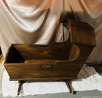 Side view of large antique wooden cradle, showcasing rocker legs, slatted front panel and canopy top detail.