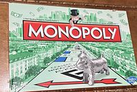 Photo of Monopoly game board with dog token and Monopoly logo featuring Mr. Monopoly on a green cityscape background.