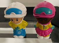 Photo of two Little People toys standing side by side on a reflective surface showing details of their helmets and clothing.