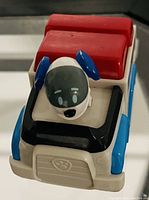 Front and side view of the Paw Patrol Chase vehicle toy, showing the character figure seated and the paw print emblem on the grill.