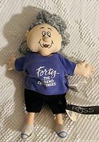 Photo of the Russ plush toy showing the full body with blue shirt, black pants, gray hair, and facial features.