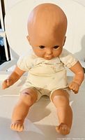 Front view of the vintage baby doll showing realistic head, painted detail, and cream clothing.