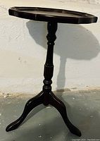 Side view of dark wood accent table showing turned single pedestal and three curved legs.