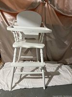 Front view of the wooden antique high chair showing the tray, rounded backrest, and turned legs.