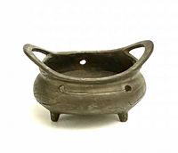 Front angled view showing the incense burner's rounded bronze body with engraved pattern, three legs, and tall loop handles.