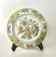 Full view of the circular porcelain plate on a wooden stand showing detailed floral and bird motifs and colorful borders.