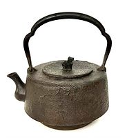 Front angled view of the antique Japanese iron teapot showing floral engravings and lion figure on lid
