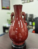 Front side view of copper red glaze vase showing one elephant head handle and glossy finish.