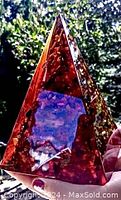 Photo showing front translucent face of the large Baltic amber pyramid held against green outdoor background.