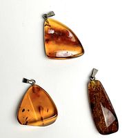 Top view of three natural Baltic amber pendants against white background showing amber inclusions and unique shapes.