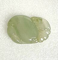 Close-up front view of pale green natural Burmese jadeite carved pendant on white background showing smooth center and carved detail at the ends.