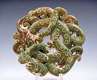 Close-up of circular reticulated jade pendant with detailed curly dragons and swirling carved patterns in green and brown jade.