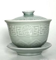 Front view of the vintage Chinese cup with lid sitting on saucer, showing detailed patterns on the cup and lid.