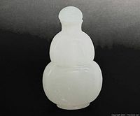 White Peking glass snuff bottle in double-gourd shape with rounded stopper, front view on dark background