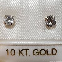 Close-up of two round white topaz gemstones in 10K white gold stud settings on a textured background showing '10 KT. GOLD' text.