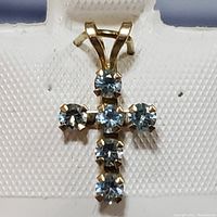 Front view of a yellow gold cross pendant with six blue topaz stones set in prongs on a textured background.
