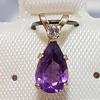 Front view of the 10K yellow gold pendant with purple amethyst pear-shaped stone and small round clear stone on top.