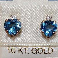 Close-up photo of pair of heart-shaped blue topaz earrings with cubic zirconia set in 10K yellow gold, displayed on a white fabric card stamped with '10 K.T. GOLD'.