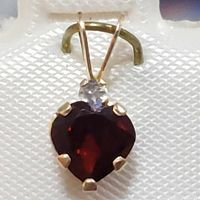 Close-up photo of 10K yellow gold heart pendant with red garnet and white accent stone, showing prong setting and bail