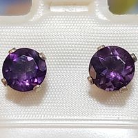 Front-facing close-up of two round faceted amethyst gemstone stud earrings set in sterling silver four-prong settings.