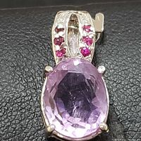 Close-up front view of sterling silver pendant with large oval purple amethyst and red ruby stones set on the bail.