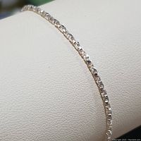 Photo showing a close-up of a slim sterling silver link chain bracelet on a white display.