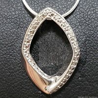 Close-up photo of the sterling silver diamond shaped pendant with diamonds around the edges on a black background.