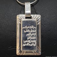 Close-up photo of the rectangular silver pendant with Arabic script engraving on a black background.